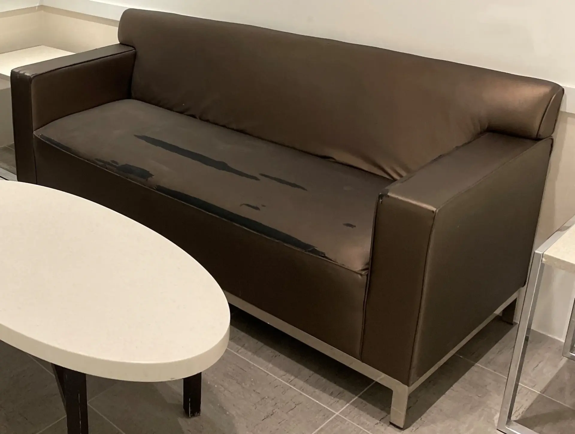 Brown upholstered sofa with extensive surface wear and peeling across the seat in a commercial seating area.