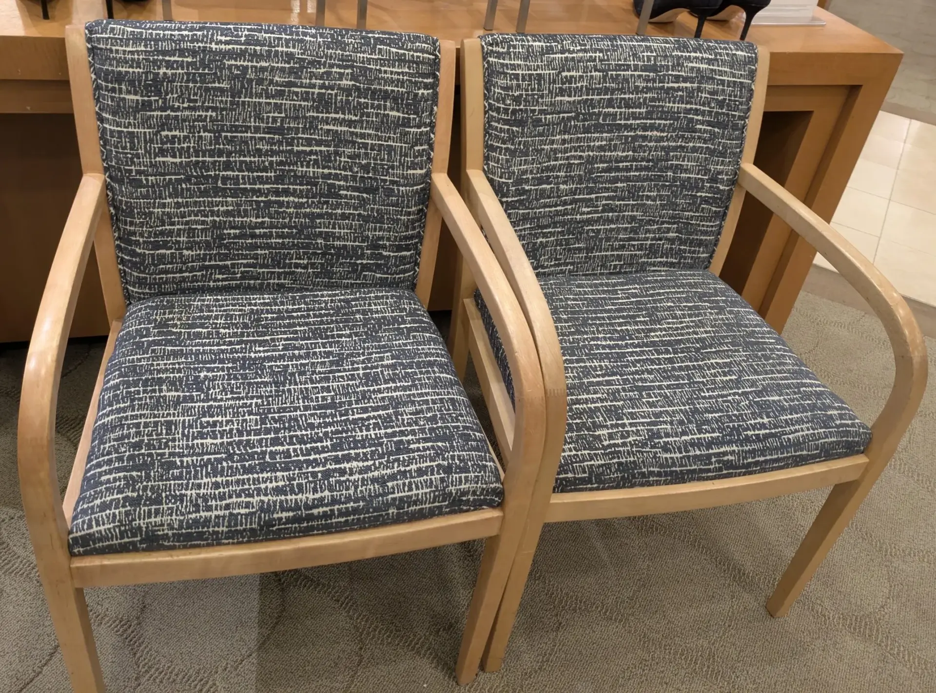 Two light wood armchairs upholstered in dark blue and white patterned fabric in a retail showroom.